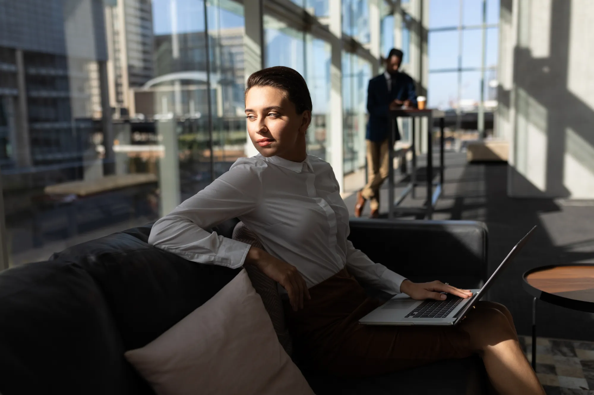 Businesswoman with laptop sitting on the sofa and looking away in office